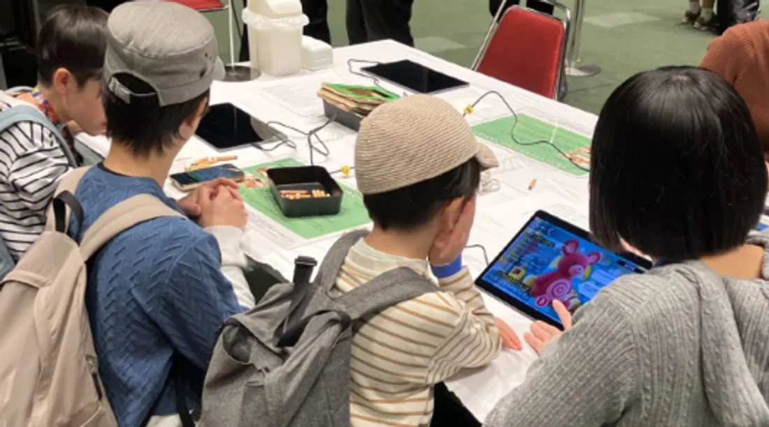 保護者と一緒にタブレットでアプリのキャラクターと会話する子ども